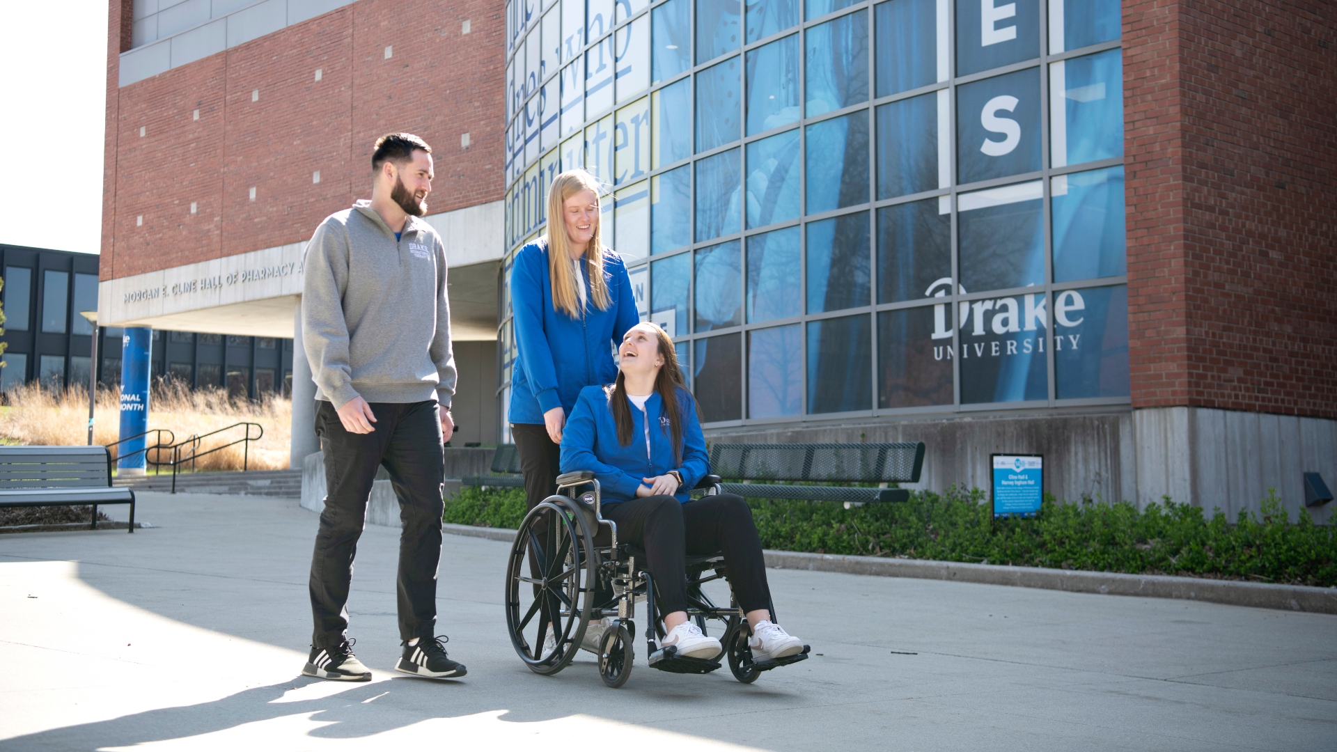 Two Drake OTD students learn more about assistive devices by pushing a classmate in a wheelchair around campus