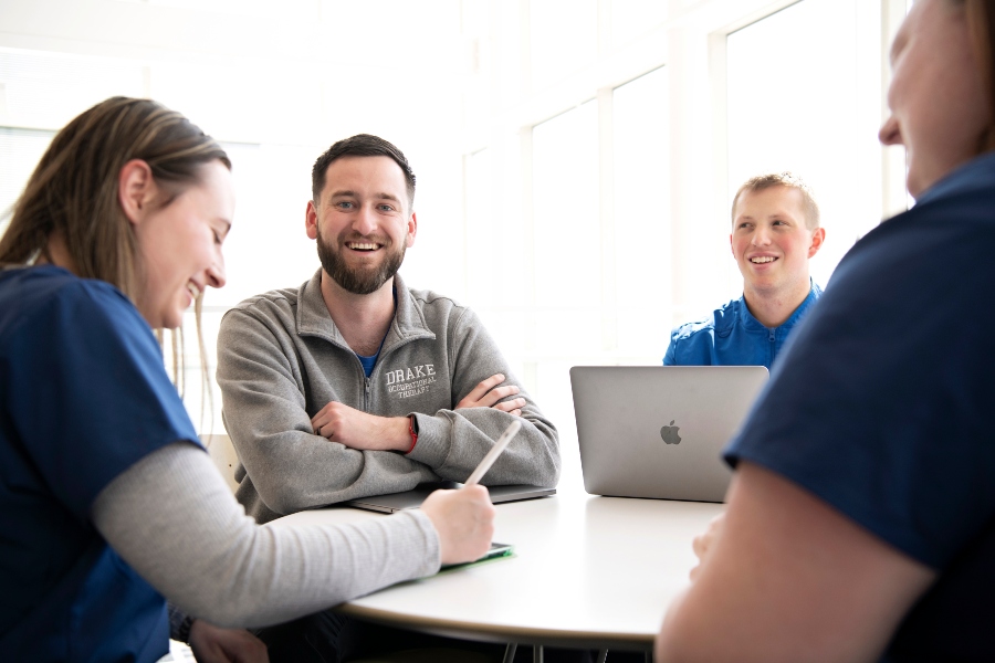 A group of OTD students with laptops sit around a table to discuss an assignment