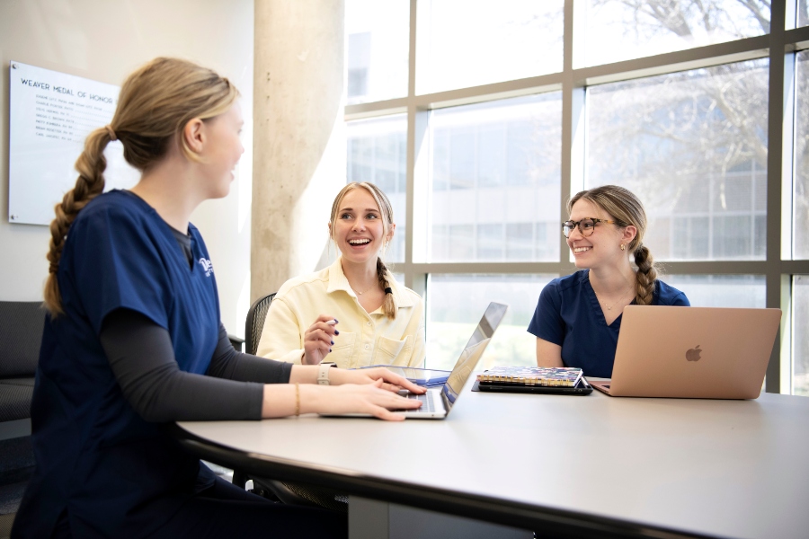 Three students in Drake's PharmD program gather around a table with their laptops to discuss career options