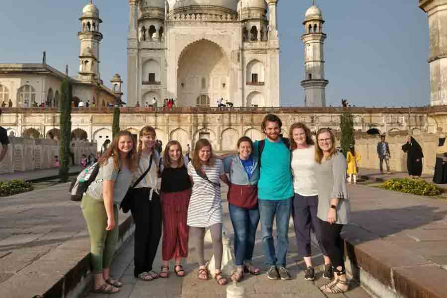 A group of Drake Philosophy students stand, arm in arm, in front of the Taj Mahal during a travel seminar trip