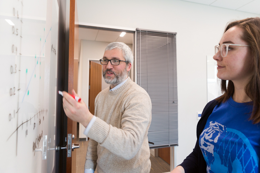 A faculty member at Drake explains a problem written on a white board to a Physics student