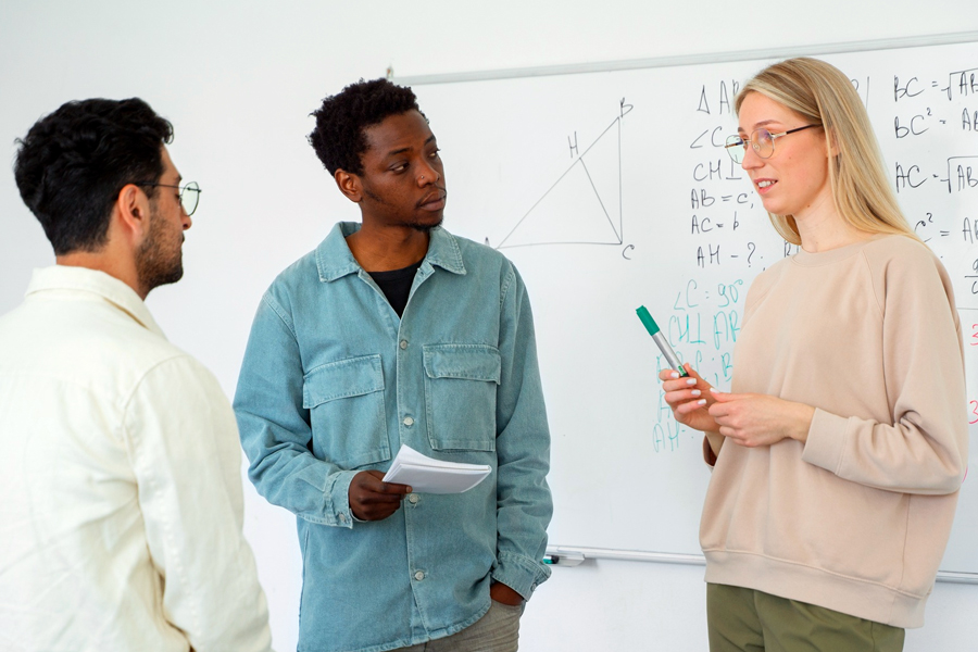 Three Drake Physics students discuss a problem integral to a research project, standing in front of a white board in a classroom