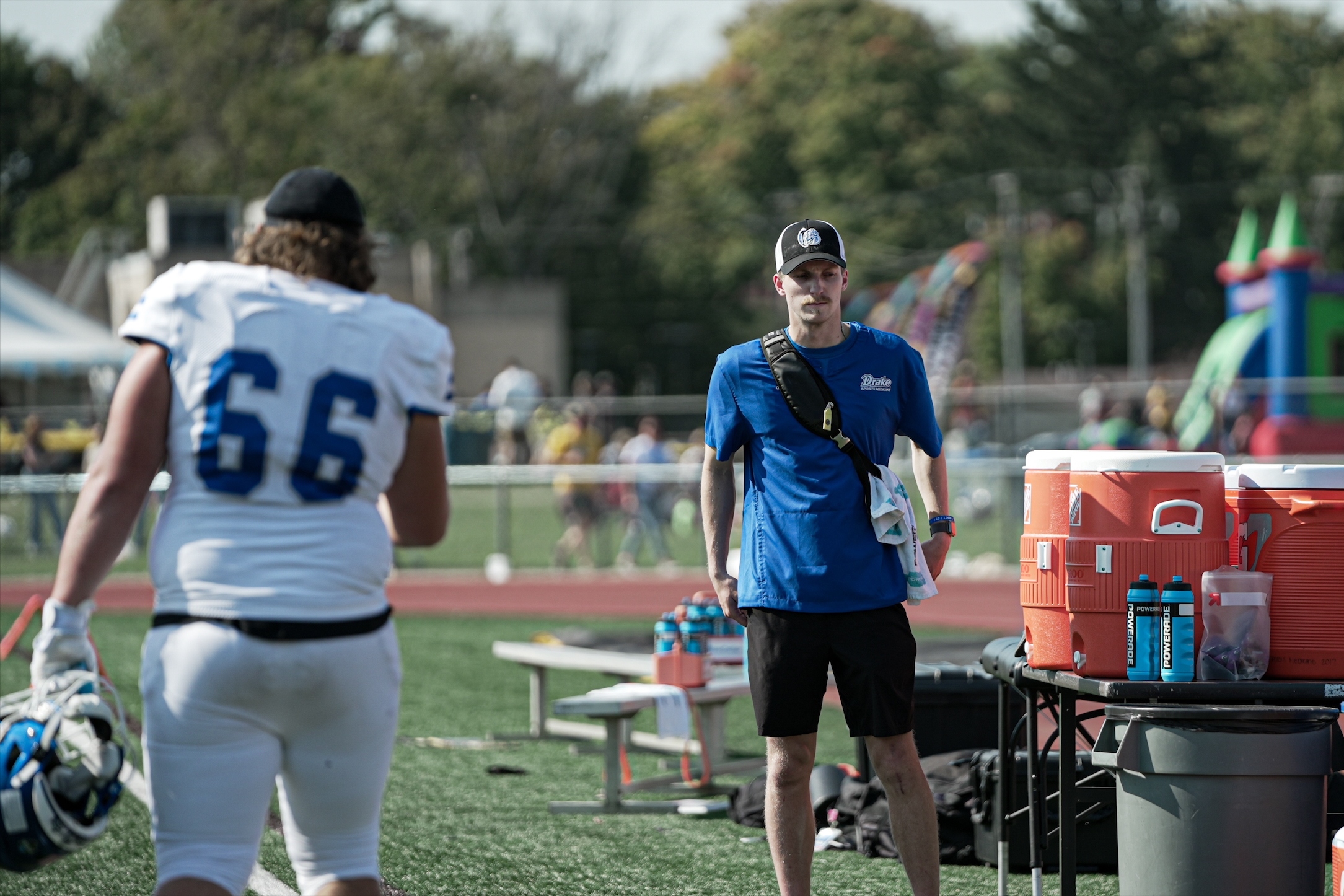 Drake Pre-Athletic Training students stand to the side of a football field to assist players during a practice