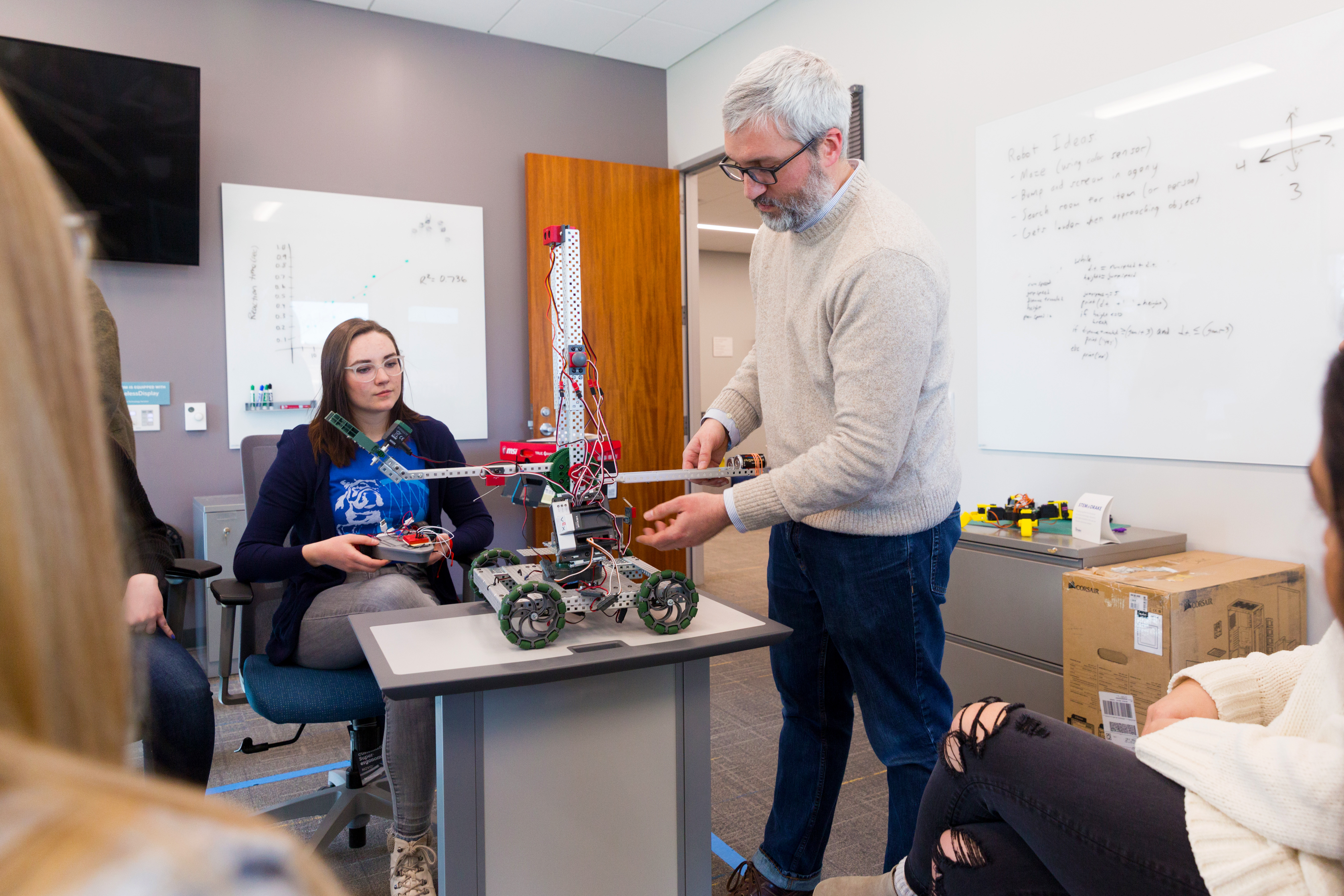 Drake Pre-Engineering students watch a professor explain electrical connections with a robot positioned on a desk