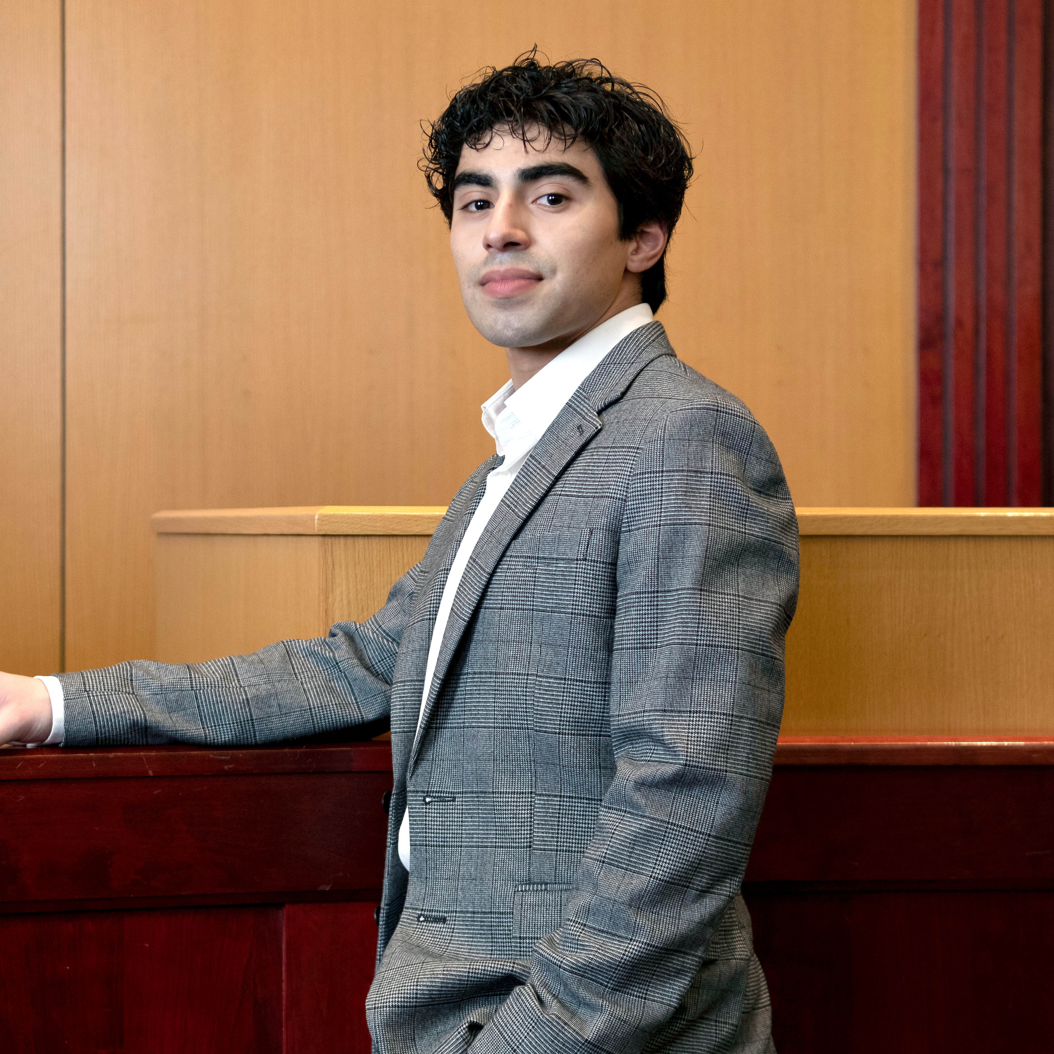 A Drake Pre-Law student in a gray suit leans against the witness stand in a courtroom setting