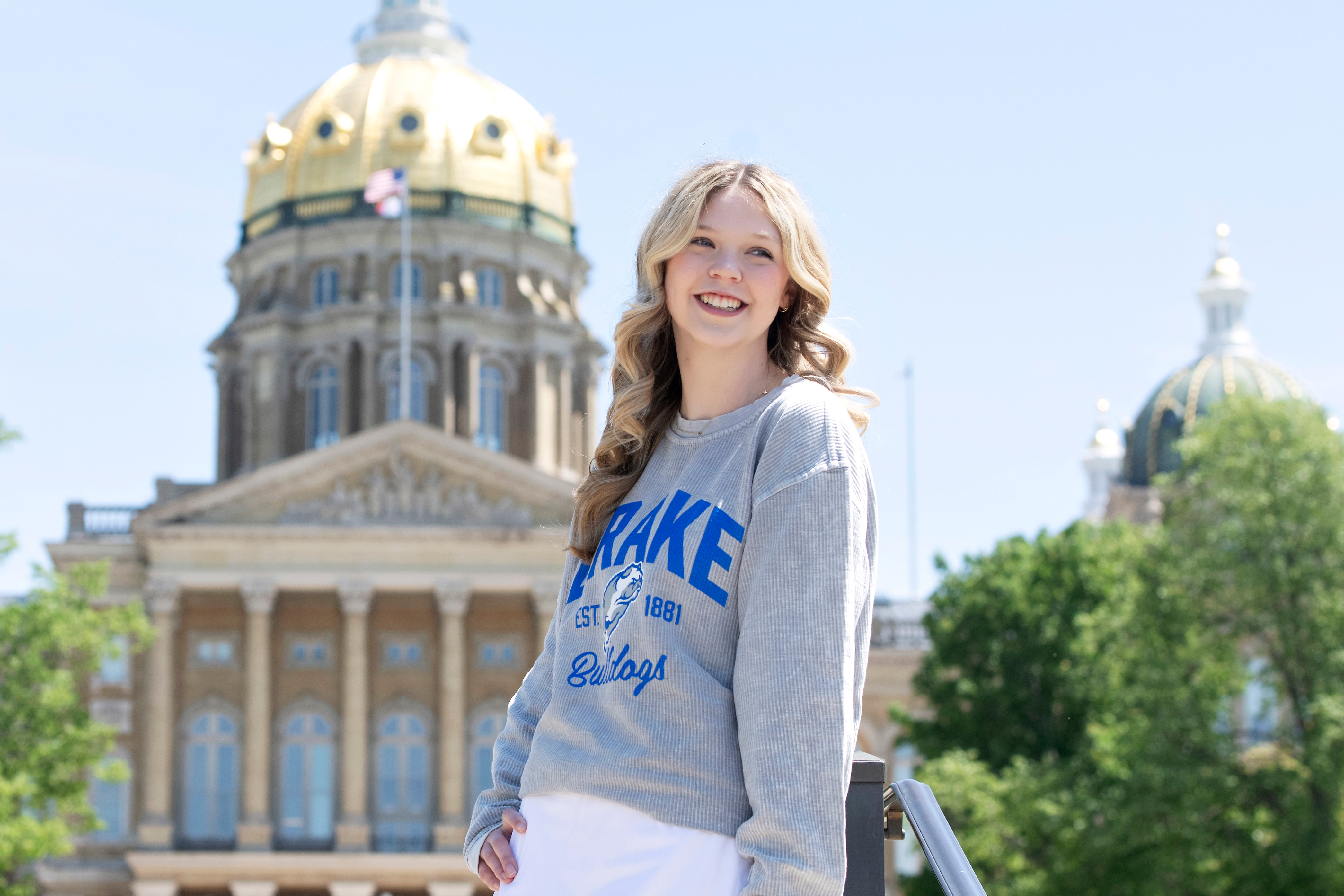 A Drake Pre-Law student in a gray Drake sweatshirt stands outside the Iowa Capitol building