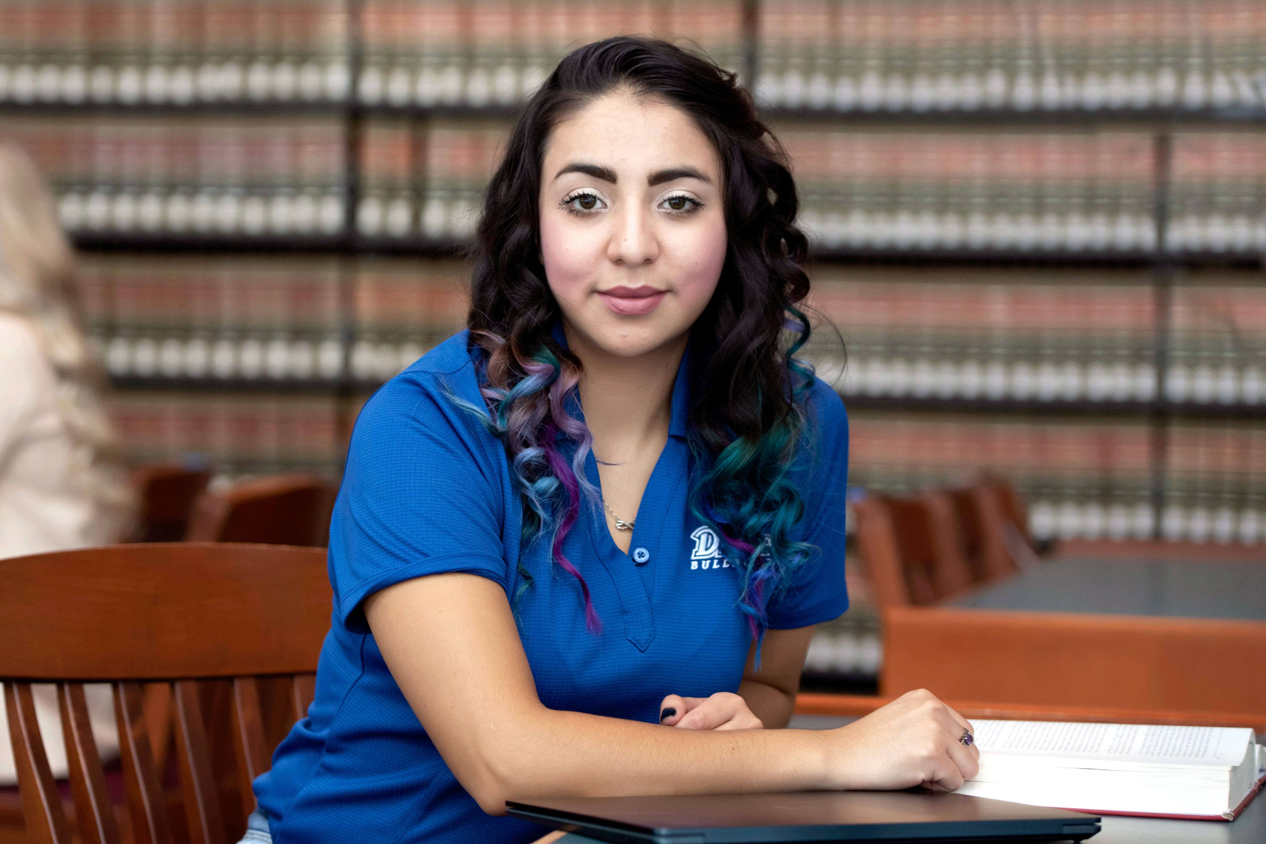 A student in a blue Drake polo shirt turns sideways while reading a book in the Drake Law library