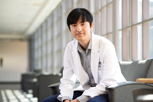 A Drake Pre-Med student in a lab coat and gingham shirt leans forward on a cushy chair in a campus common area