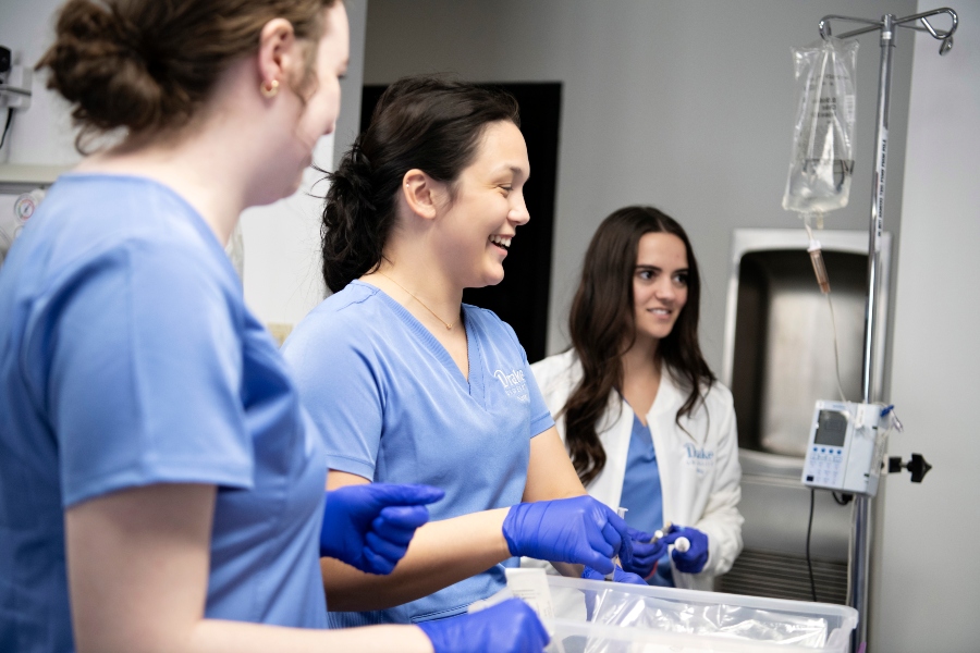 Three Drake Pre-Med students wearing scrubs learn to administer an IV in a campus simulation facility before starting their internships