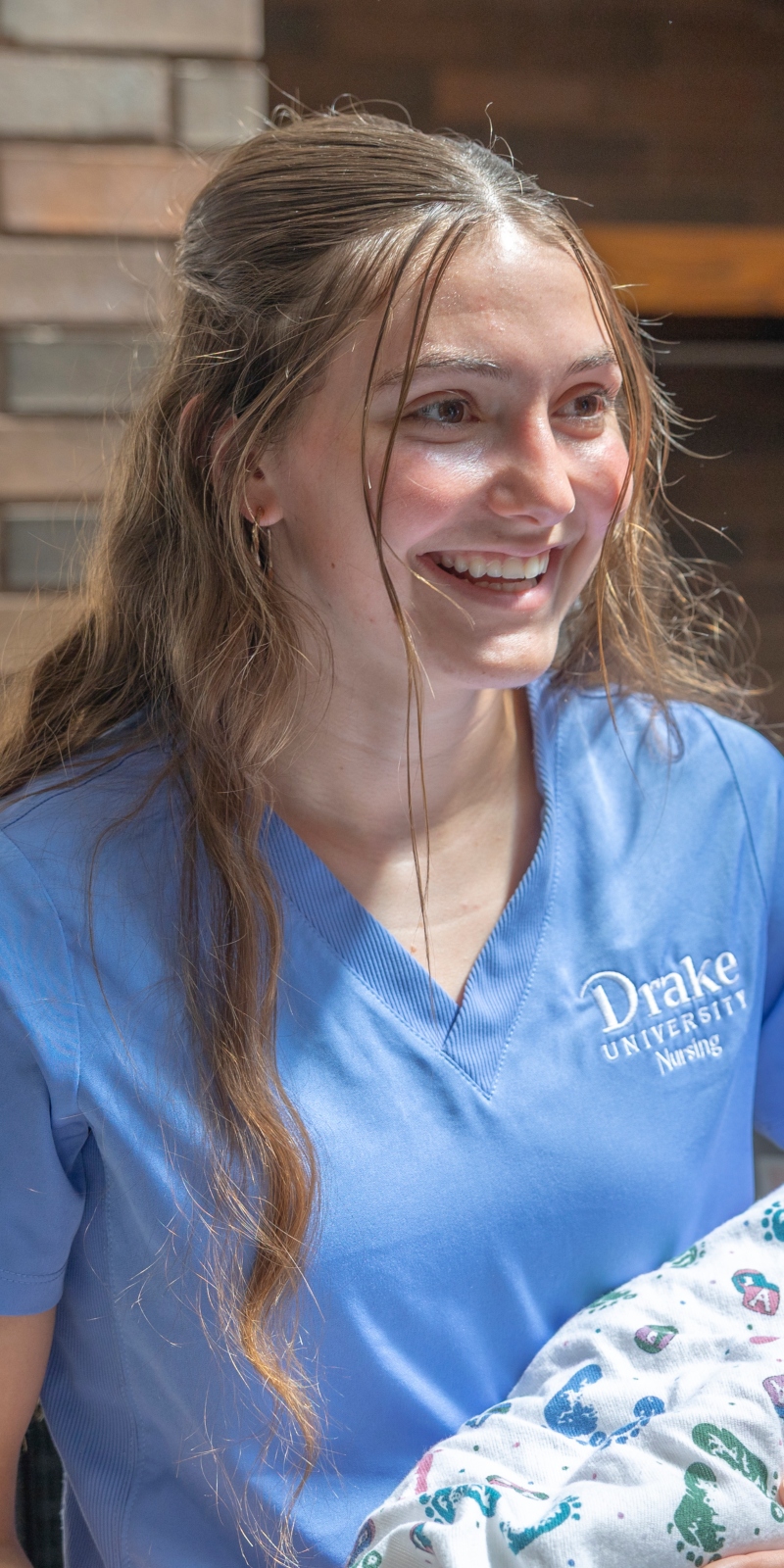 Drake Pre-Nursing alum Meghan Coulter, ABSN‘25, smiles while holding an infant manikin