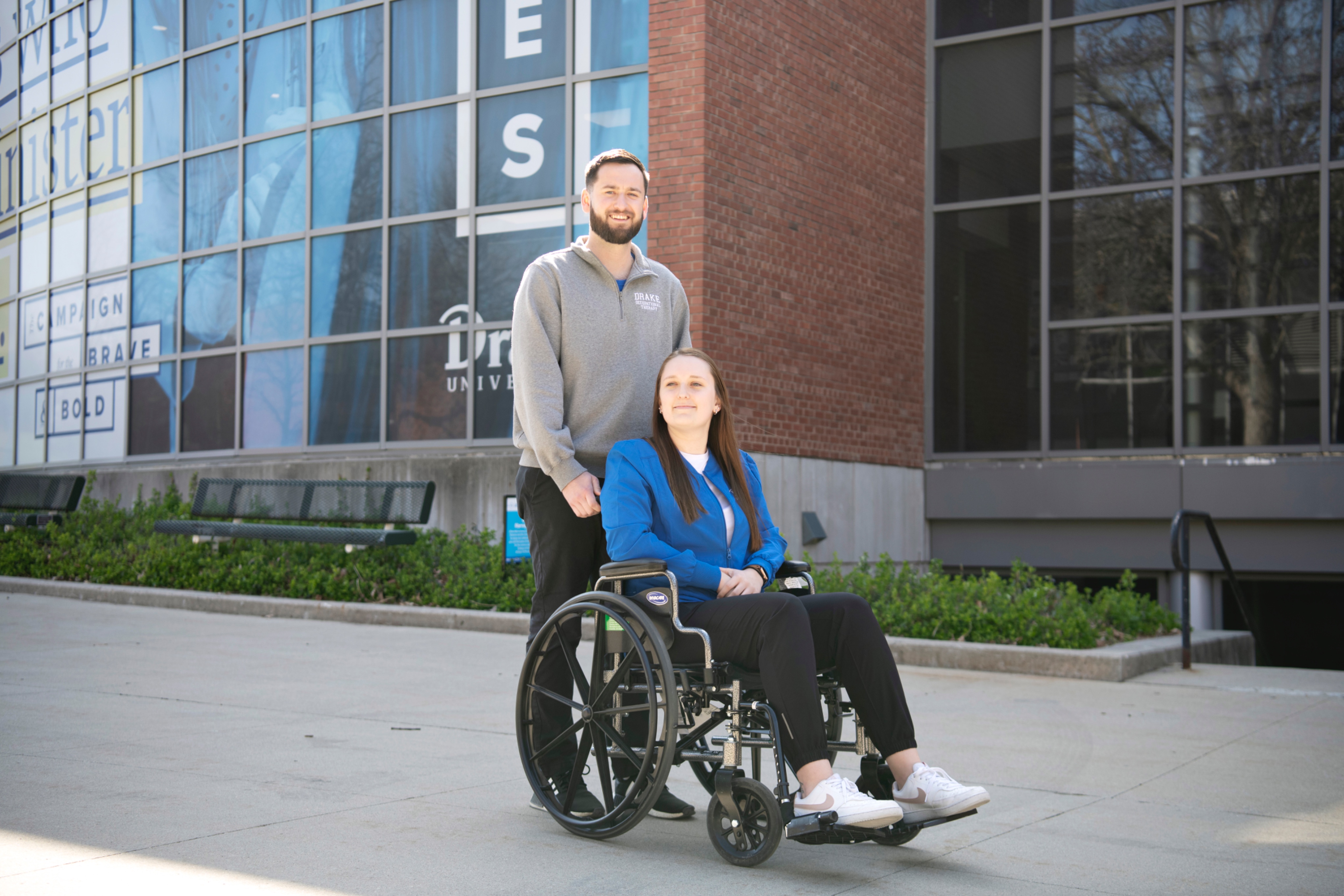 A Drake Pre-Occupational Therapy student pushes a classmate in a wheelchair around campus to learn how to use an assistive device