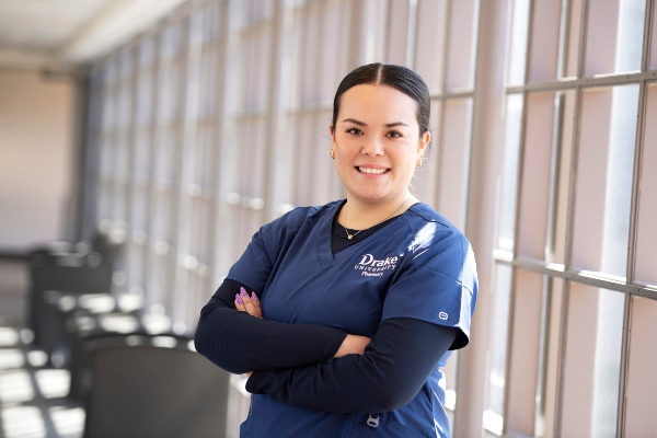 A Drake Pre-Pharmacy student in scrubs folds their arms while standing in a campus common area