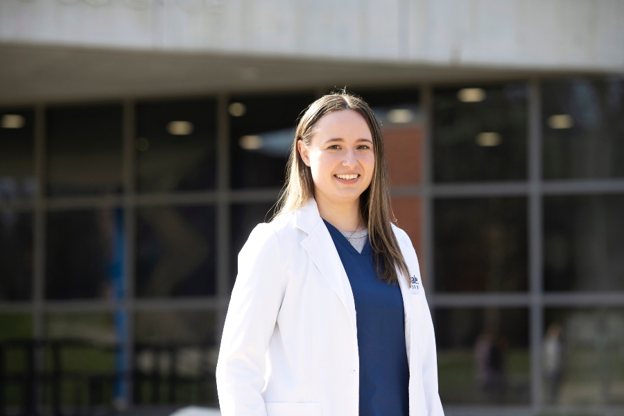 A Drake Pre-Pharmacy student in a lab coat stands outside in front of a classroom building