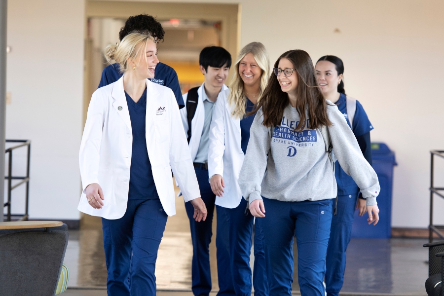 A group of Drake Pre-Pharmacy students in school garb and lab coats walk between classes