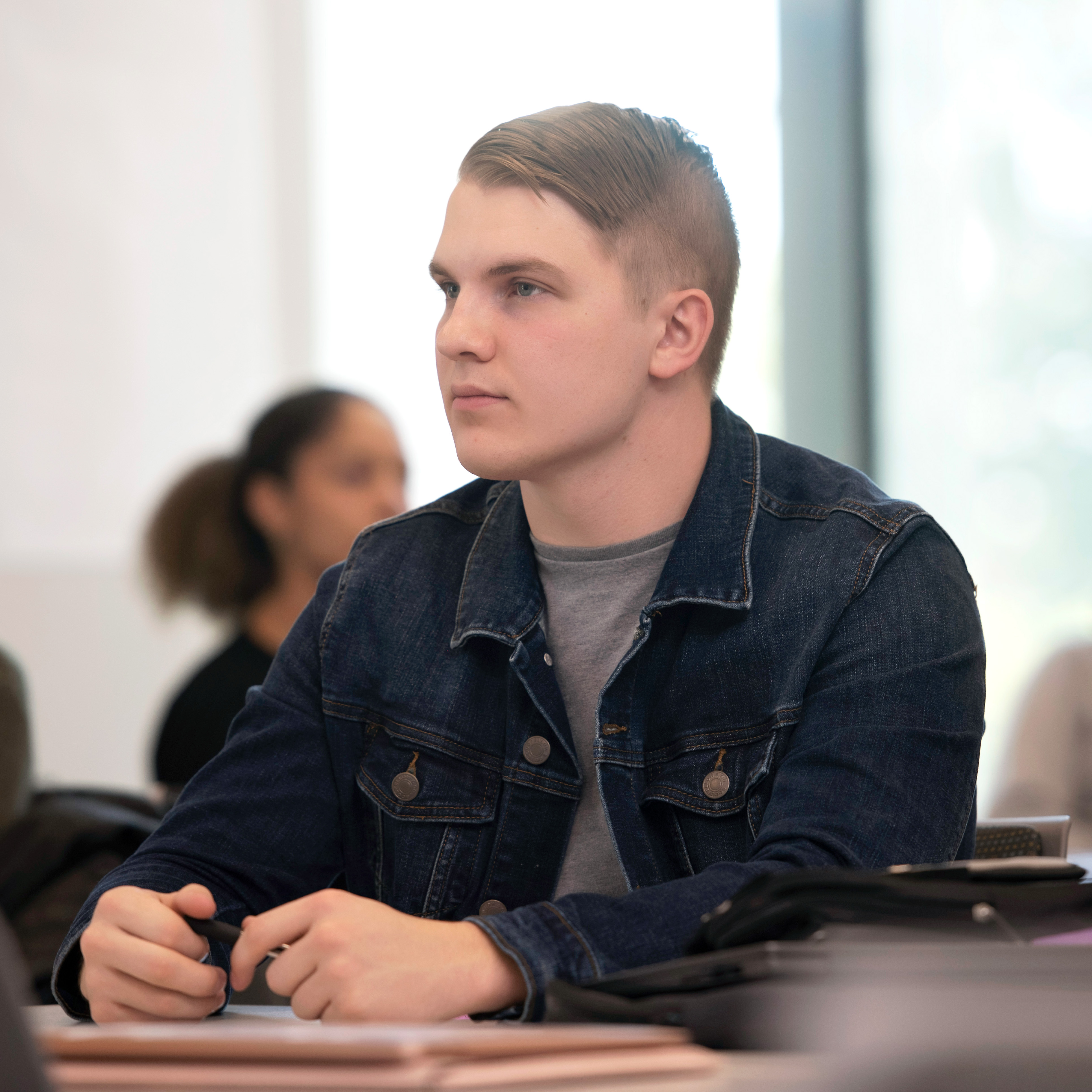 A Drake student, sitting behind a desk, focuses on the front of the classroom during a lecture