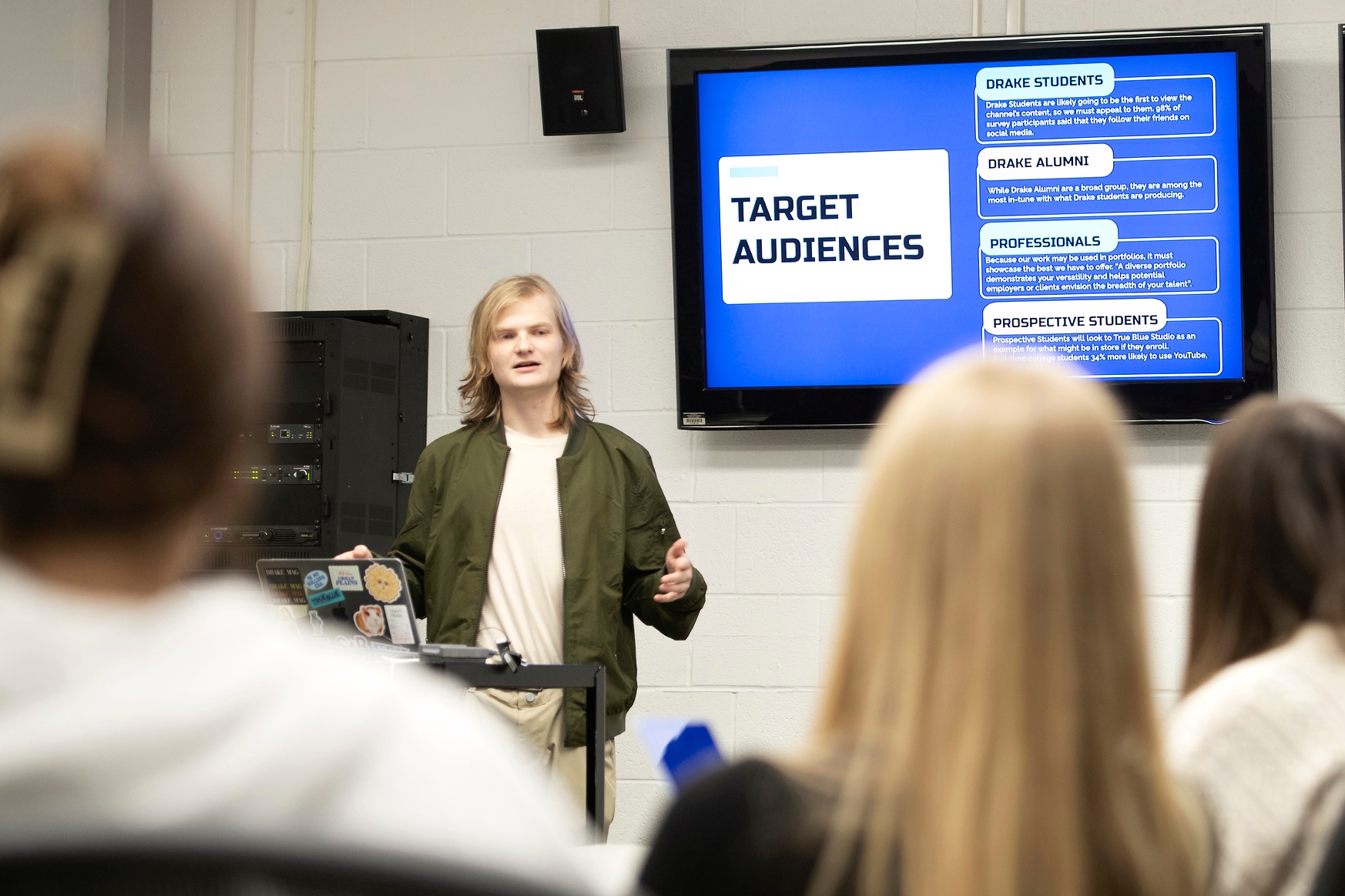 A Drake Public Relations student presents the solution their team drew up for a real-world client while standing in front of a screen with a slide presentation