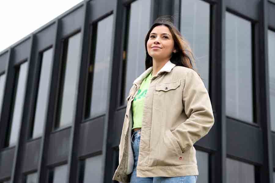 A Drake journalism student goes through a walk through campus, passing by the corner of a black building with large windows