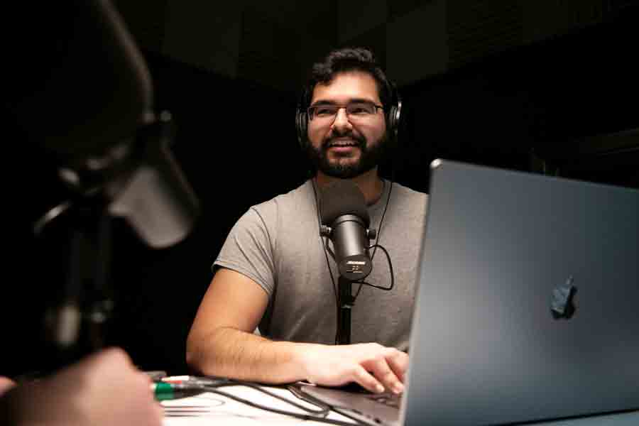 A Public Relations student runs a podcast, using a microphone and laptop in one of Drake's media labs