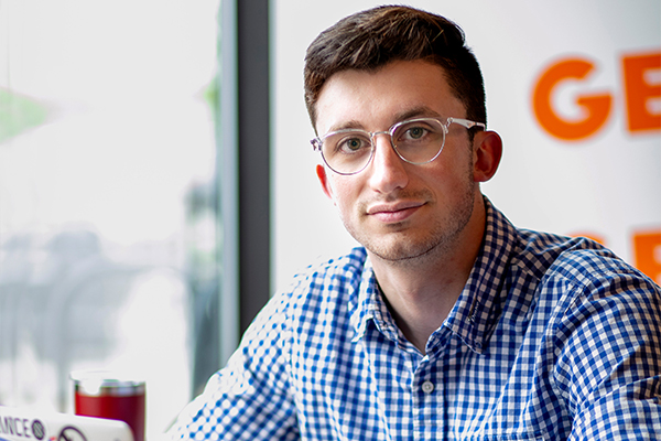 A Drake Quantitative Economics Major in glasses and a gingham check shirt sits near a window