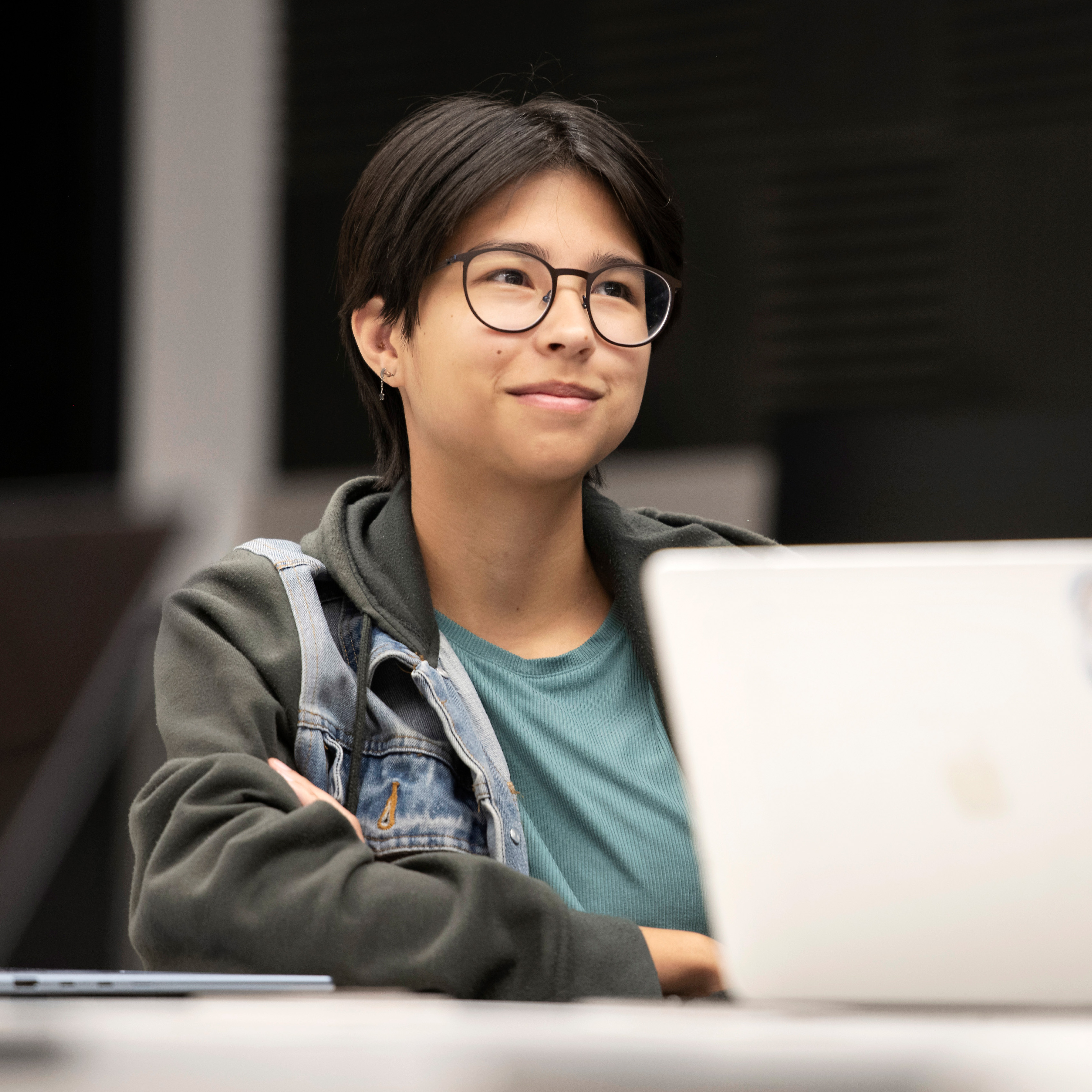 A Drake Religious and Interfaith Studies student in glasses and a denim jacket leans back during a classroom lecture