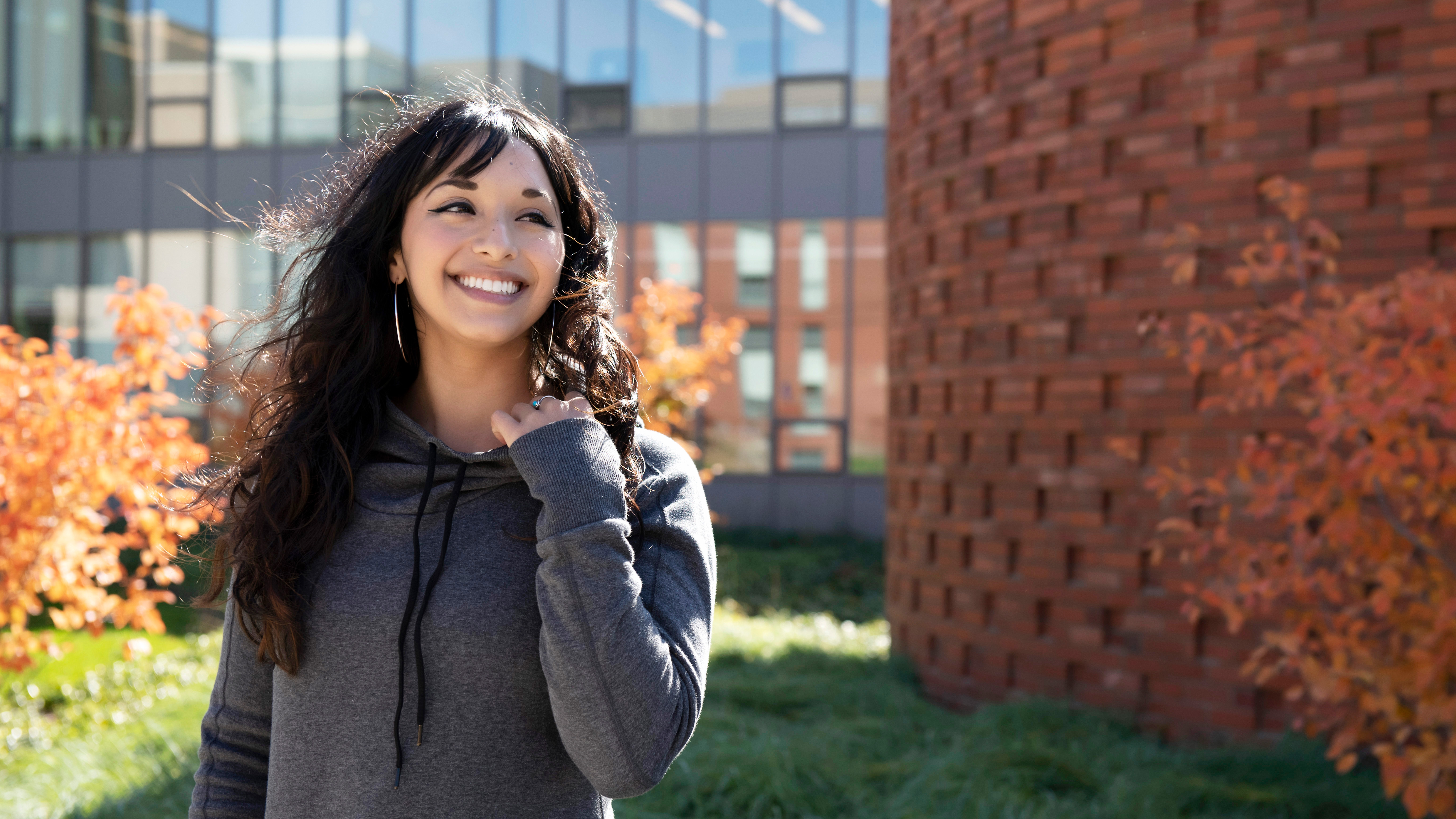 A Drake Religious and Interfaith Studies student wearing a gray hoodie stands in front of a red brick building on a windy day