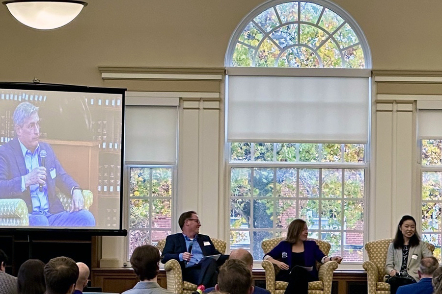 During the Drake Risk and Opportunity Forum, three insurance industry professionals sit in armchairs to discuss their field, while a virtual speaker appears on a screen behind