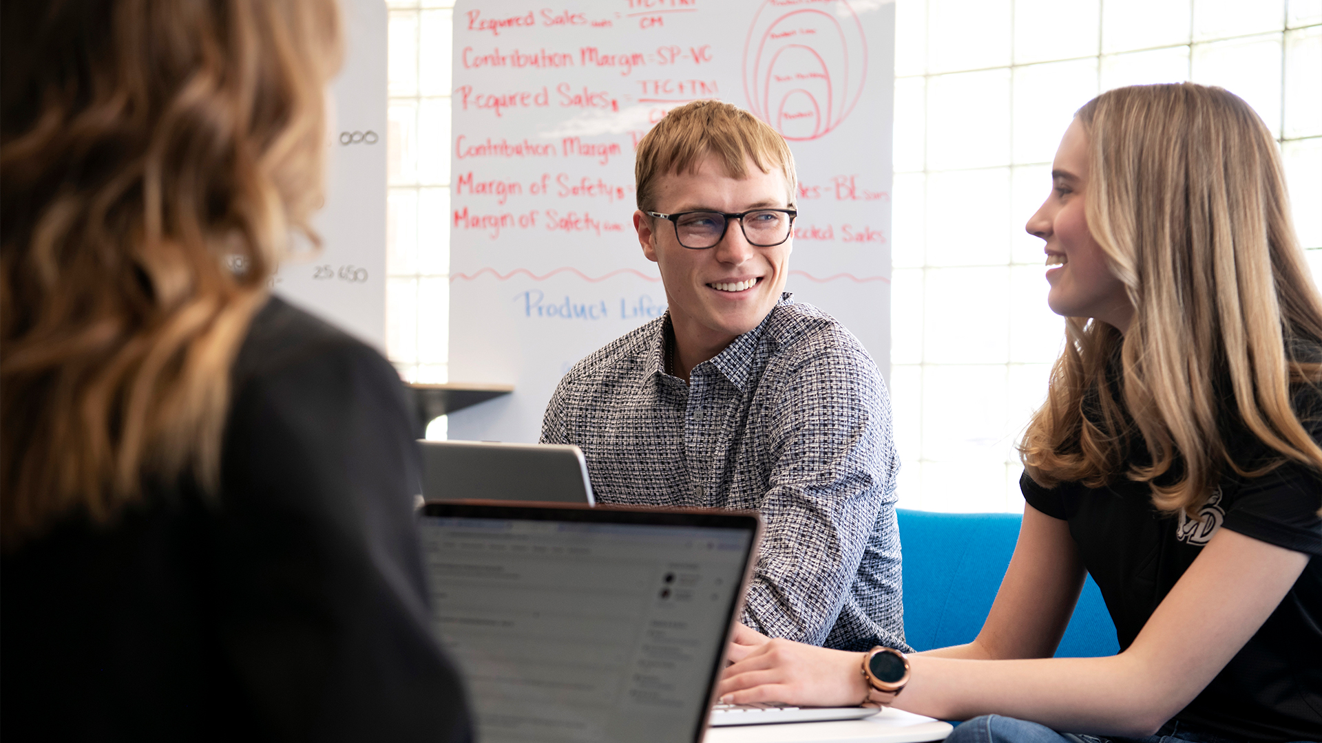 Three Risk Management and Insurance minors at Drake discuss a project around a table, with notes written on a whiteboard in the background