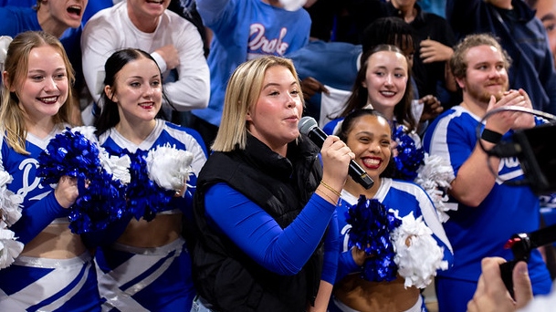 A student from Drake's Sports Media and Communication program speaks into a microphone in front of a group of cheerleaders