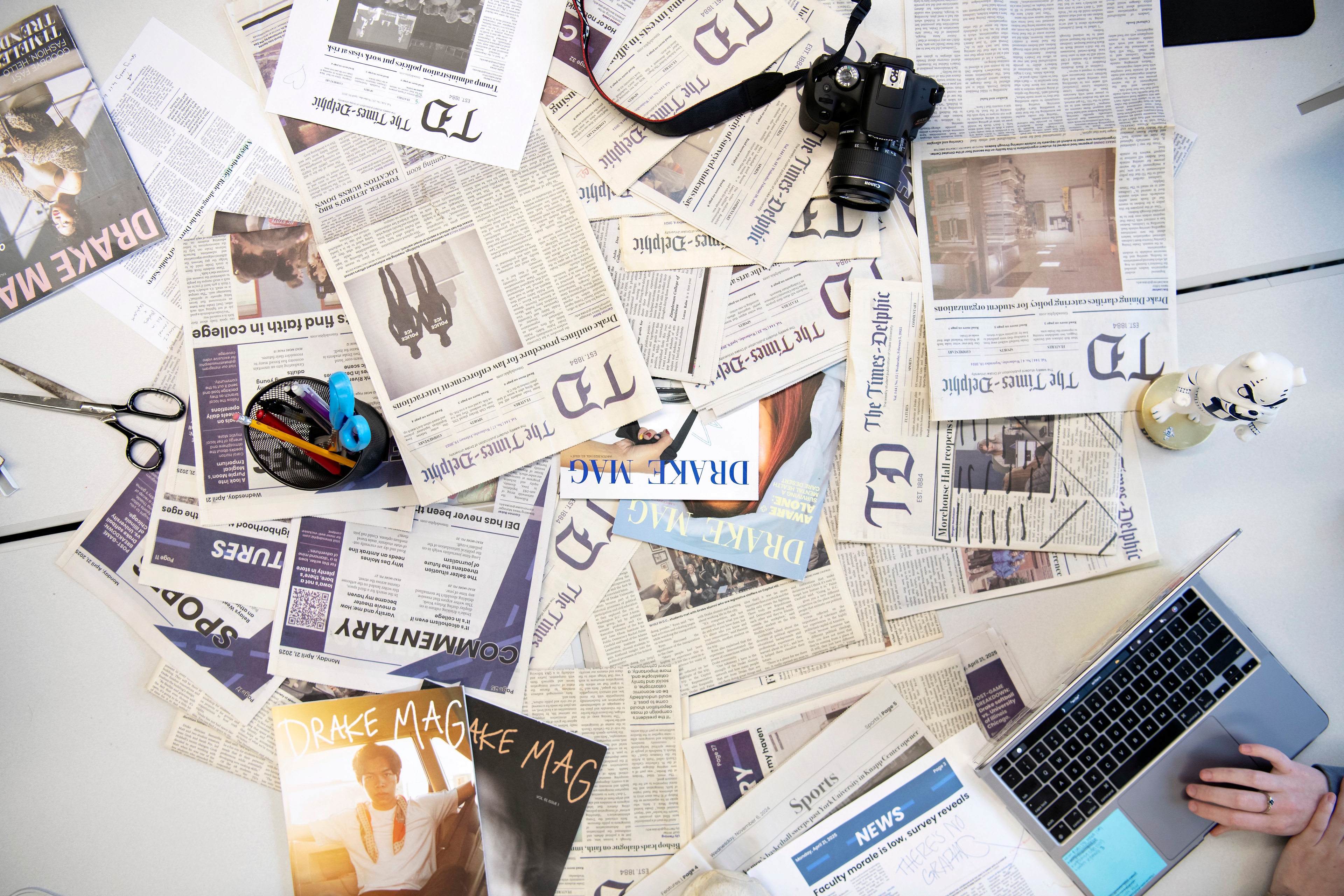 A student on a laptop works near an arrangement of publications opens to students in Drake's Sports Media and Communication program