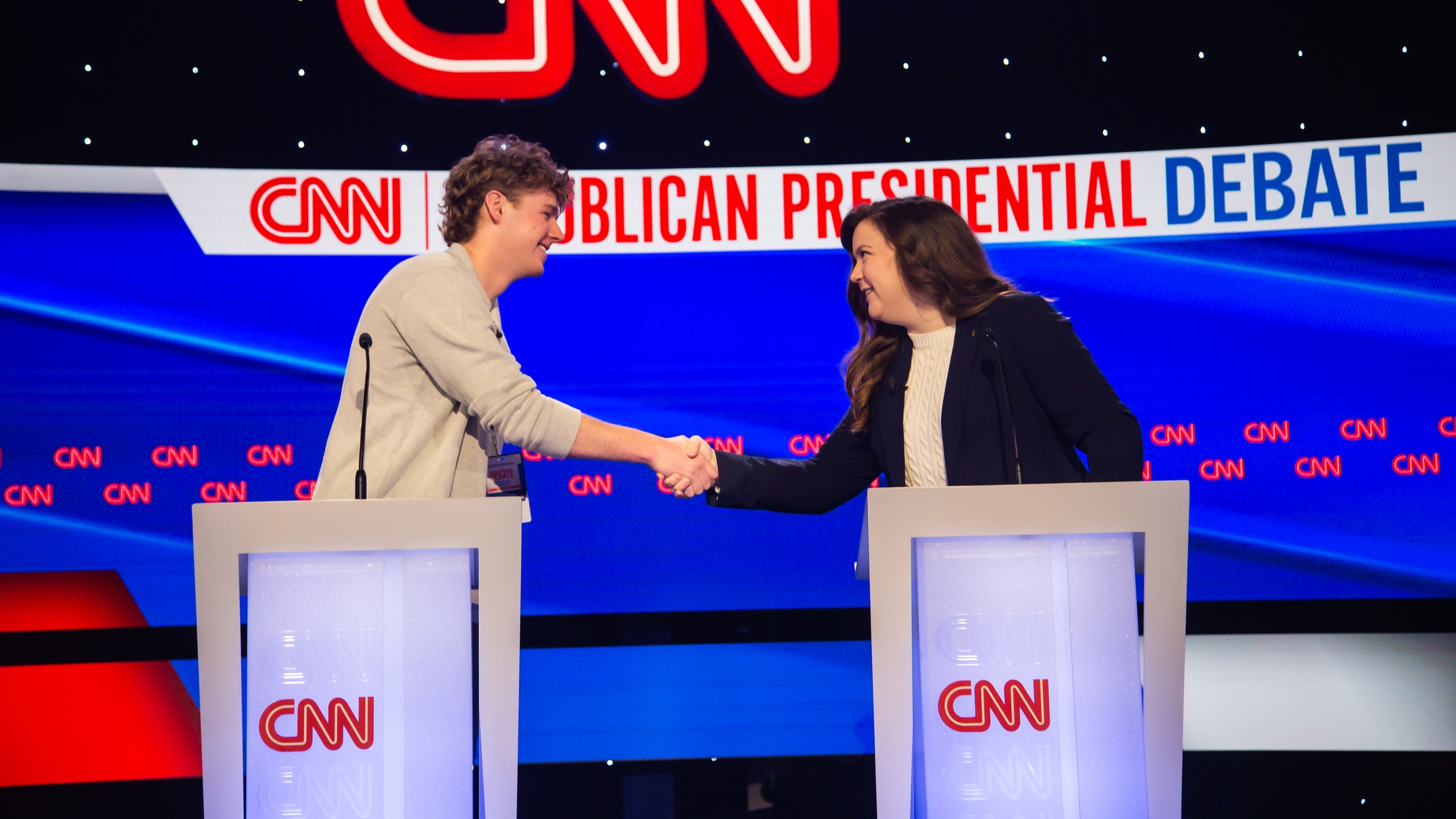 A Drake Strategic Political Communication students shakes hands with a communications professional behind a podium where CNN will be broadcasting the Republican Primary Debate 