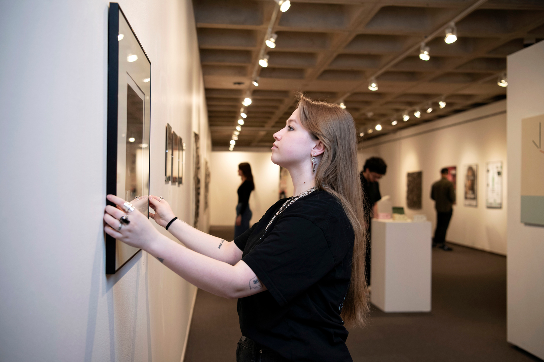 A Drake Studio Art student adjusts a picture in a campus gallery ahead of an exhibit