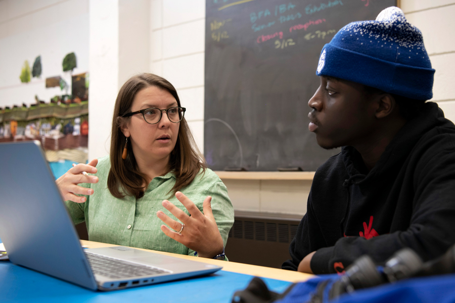 A faculty member provides feedback to a Drake Studio Art student who is seated behind a laptop