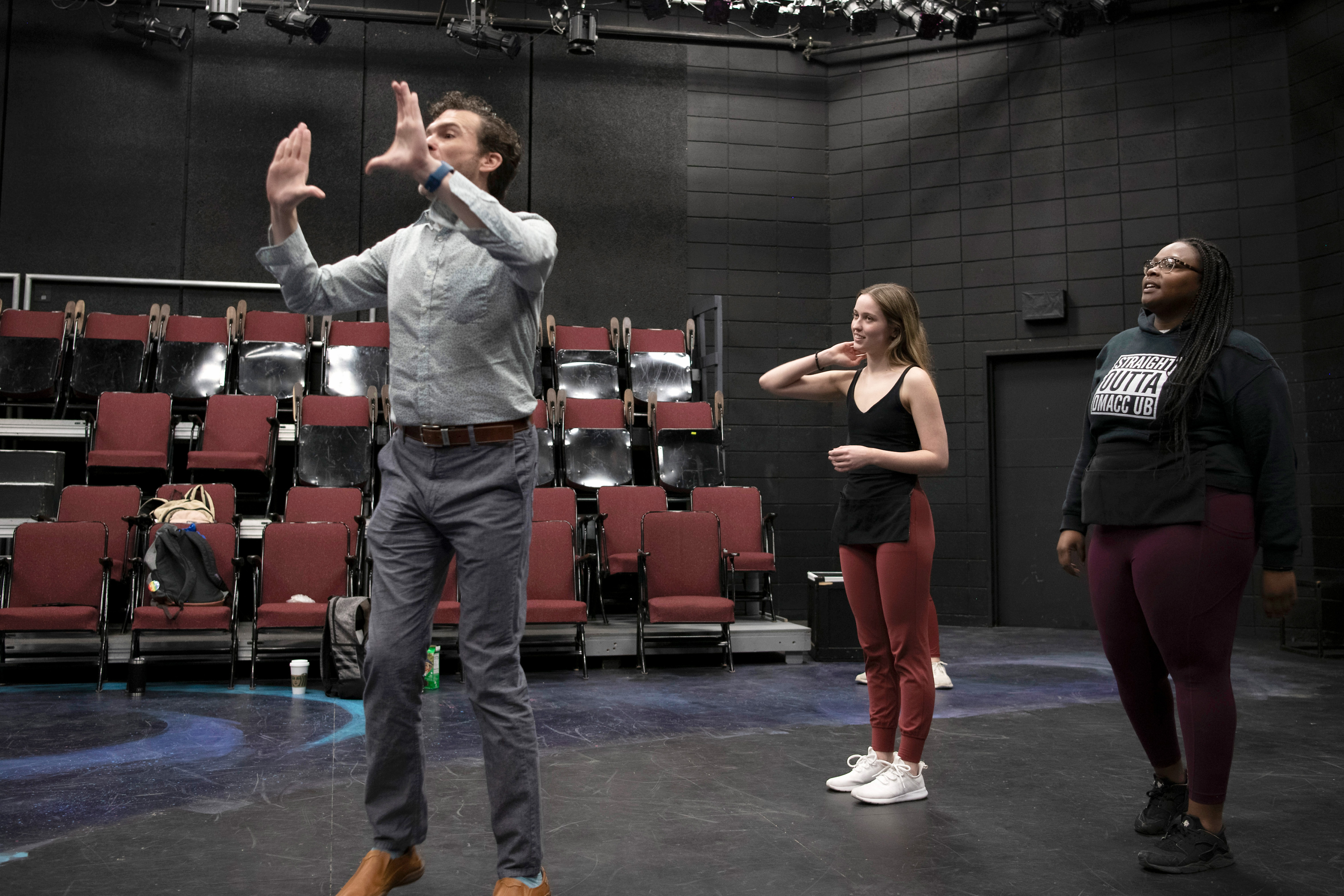 In a black box theatre on the Drake campus, a faculty member gestures while directing two students standing behind