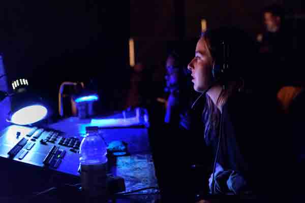 A Drake Theatre Major wearing a headset operates a soundboard during a campus production