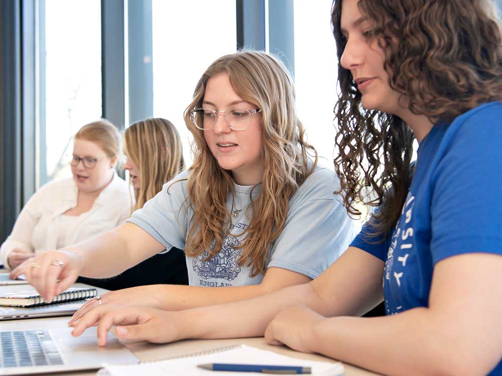Four students sitting at a table talking in a classroom.