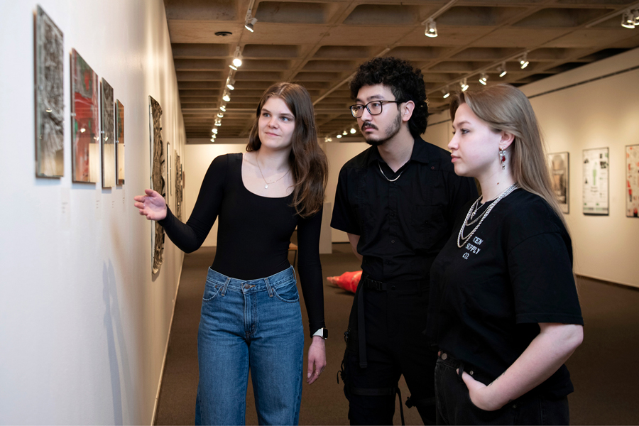 Three students look at art pieces on the wall of an art gallery