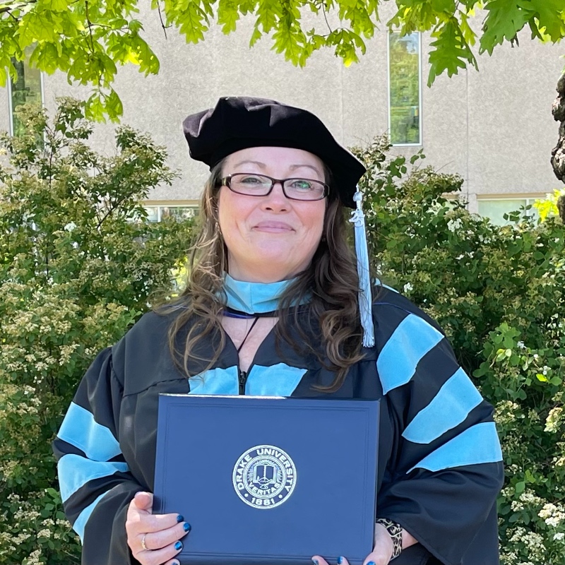 An EdD graduate in academic regalia holding her doctoral degree and smiling