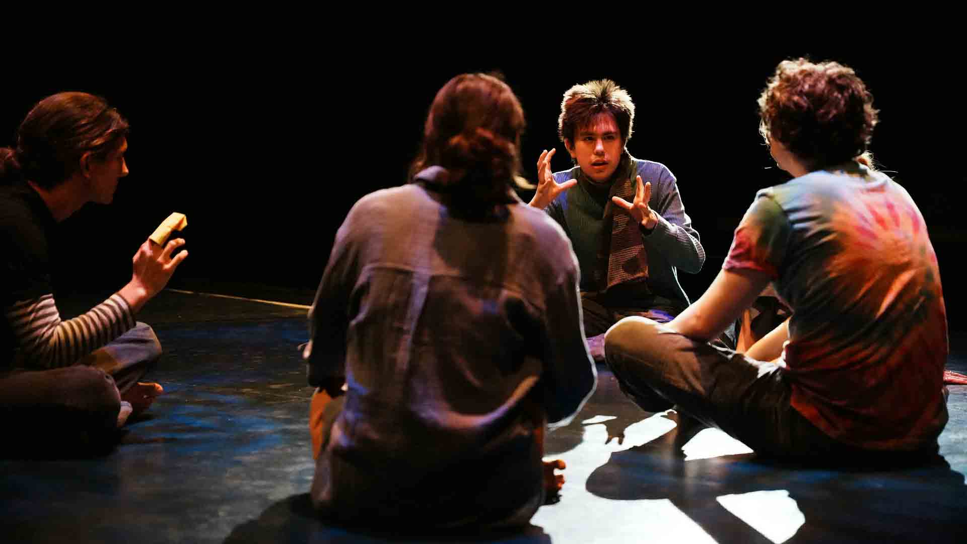 A group of four students sitting on a stage in dim lighting