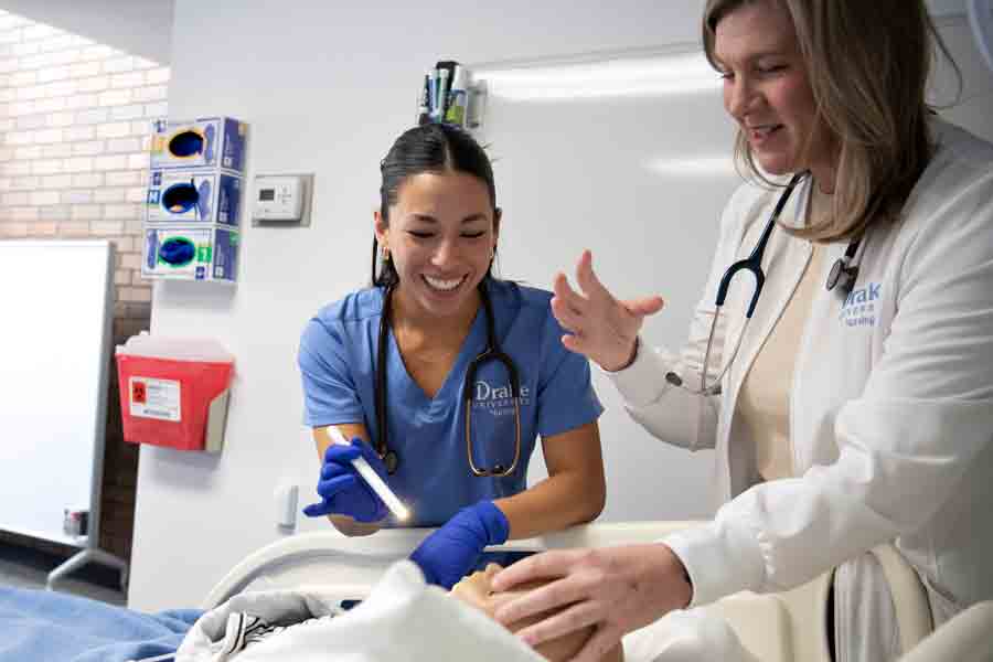 A student and a professor smile while working on a mannikin in a medical setting