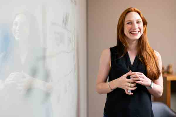 A student smiles while presenting a lesson in front of a whiteboard