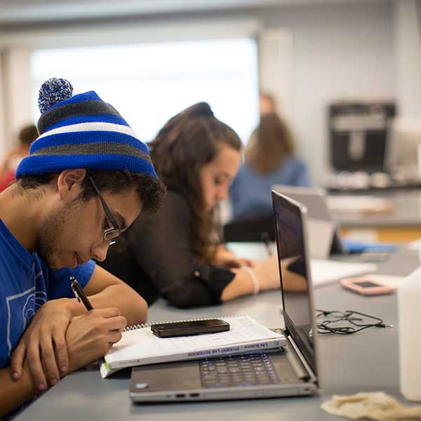 Student sitting at a lab table taking notes in front of a laptop.