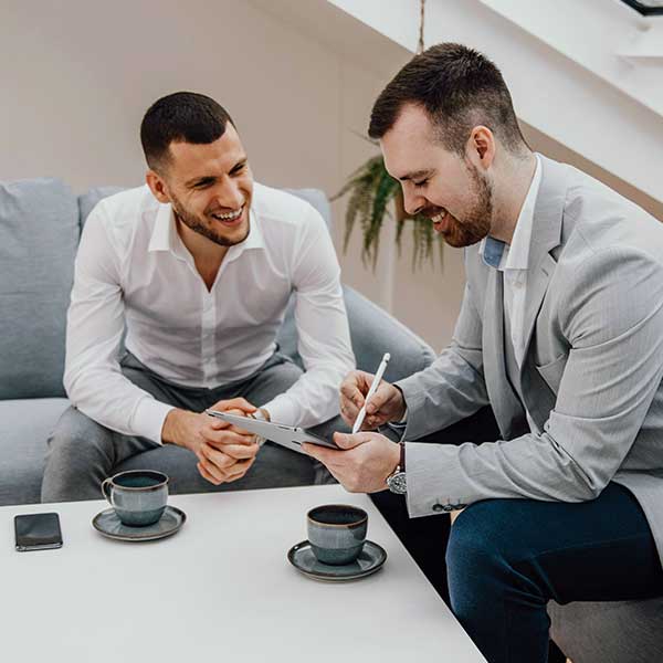 Two men sitting together looking at an iPad.