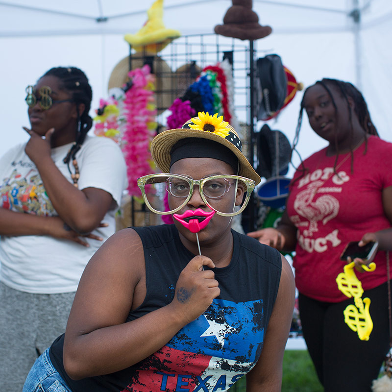 Three Drake University students posing with props at a photo booth outside on campus