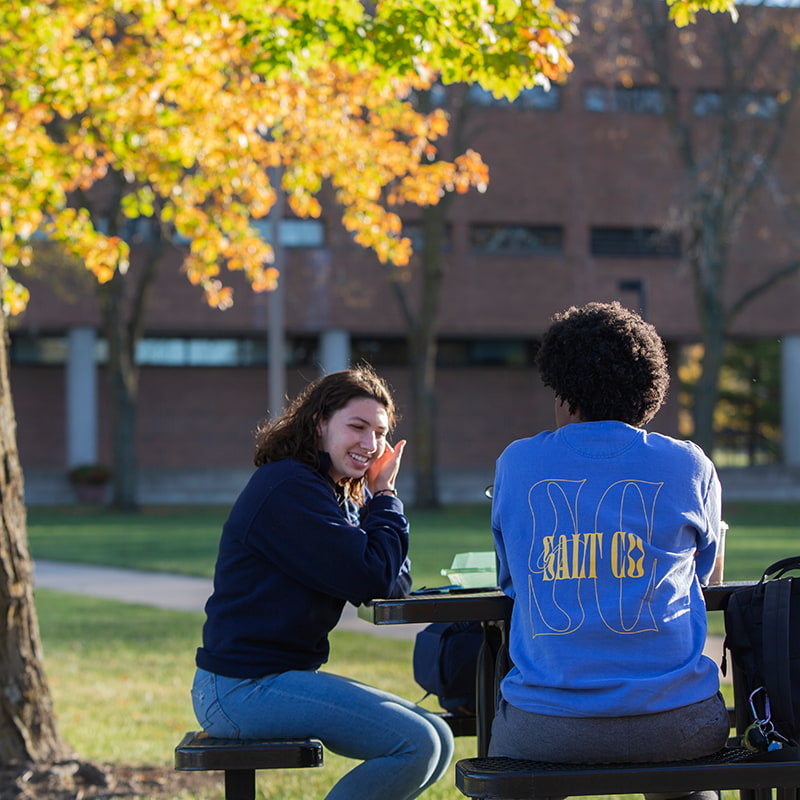 Two Drake University students sitting on a bench outside on campus talking