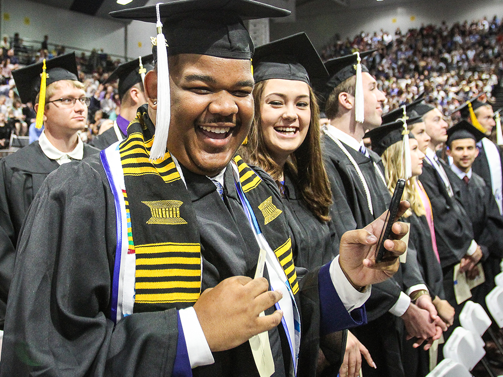 A group of student smiling and laughing together in their regalia at a Drake University Commencement ceremony.