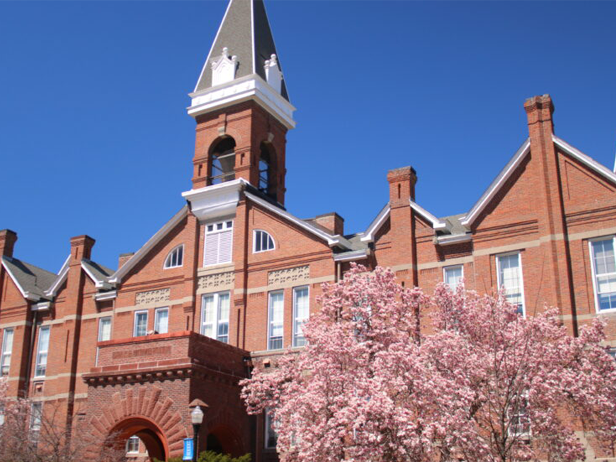 Exterior of Old Main in the spring with a flowering tree in the foreground.